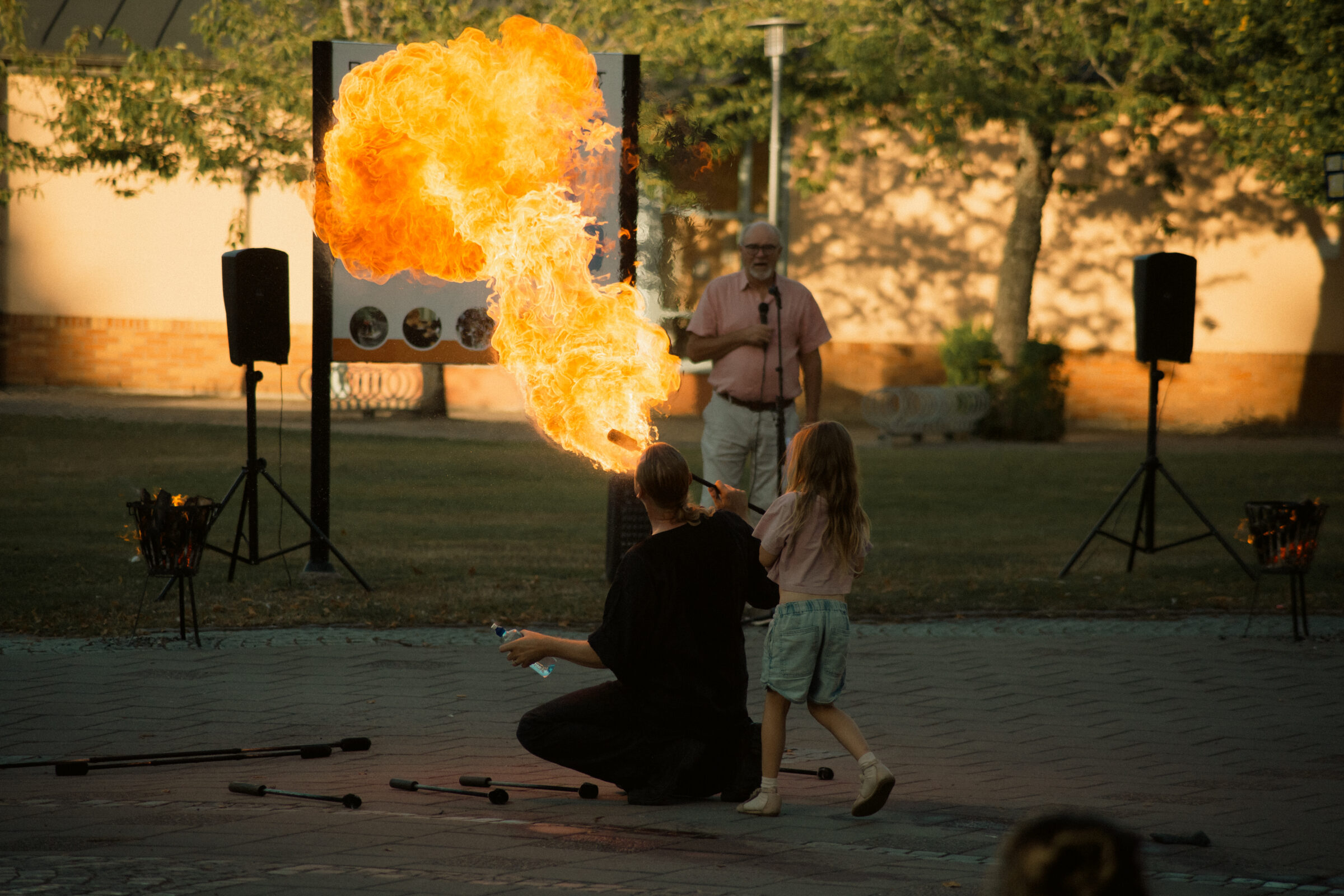 En person sprutar eld på en uppvisning, ett barn står bakom.